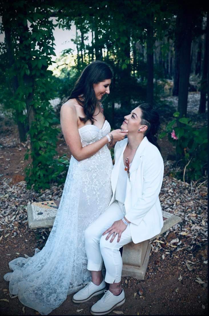 Two brides in a woodland garden, one with long dark waves and soft glam makeup