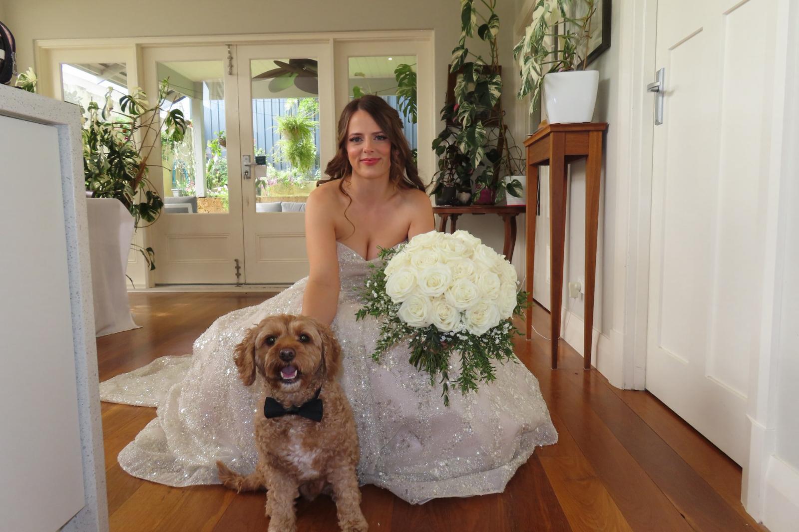 Emma in a sparkling bridal gown with soft waves, sitting with her dog and her bouquet