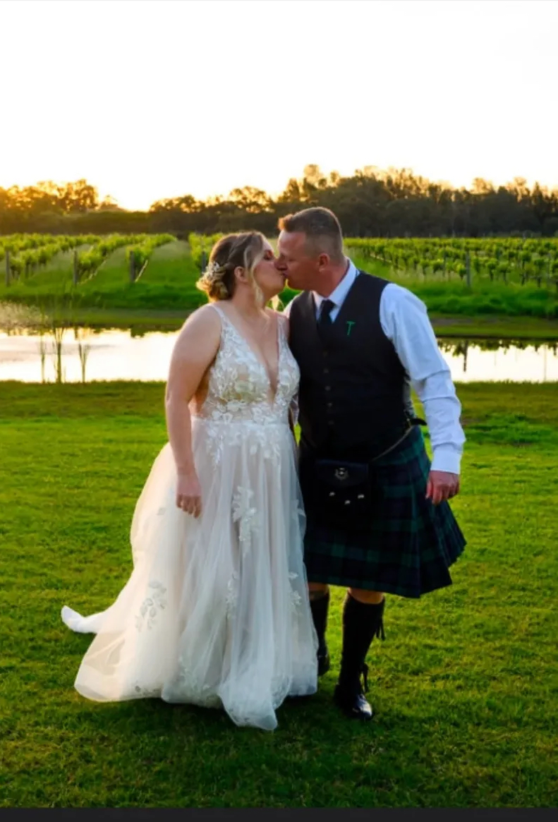 Real bride kissing her groom at sunset in a vineyard, soft blonde updo with a hairpiece