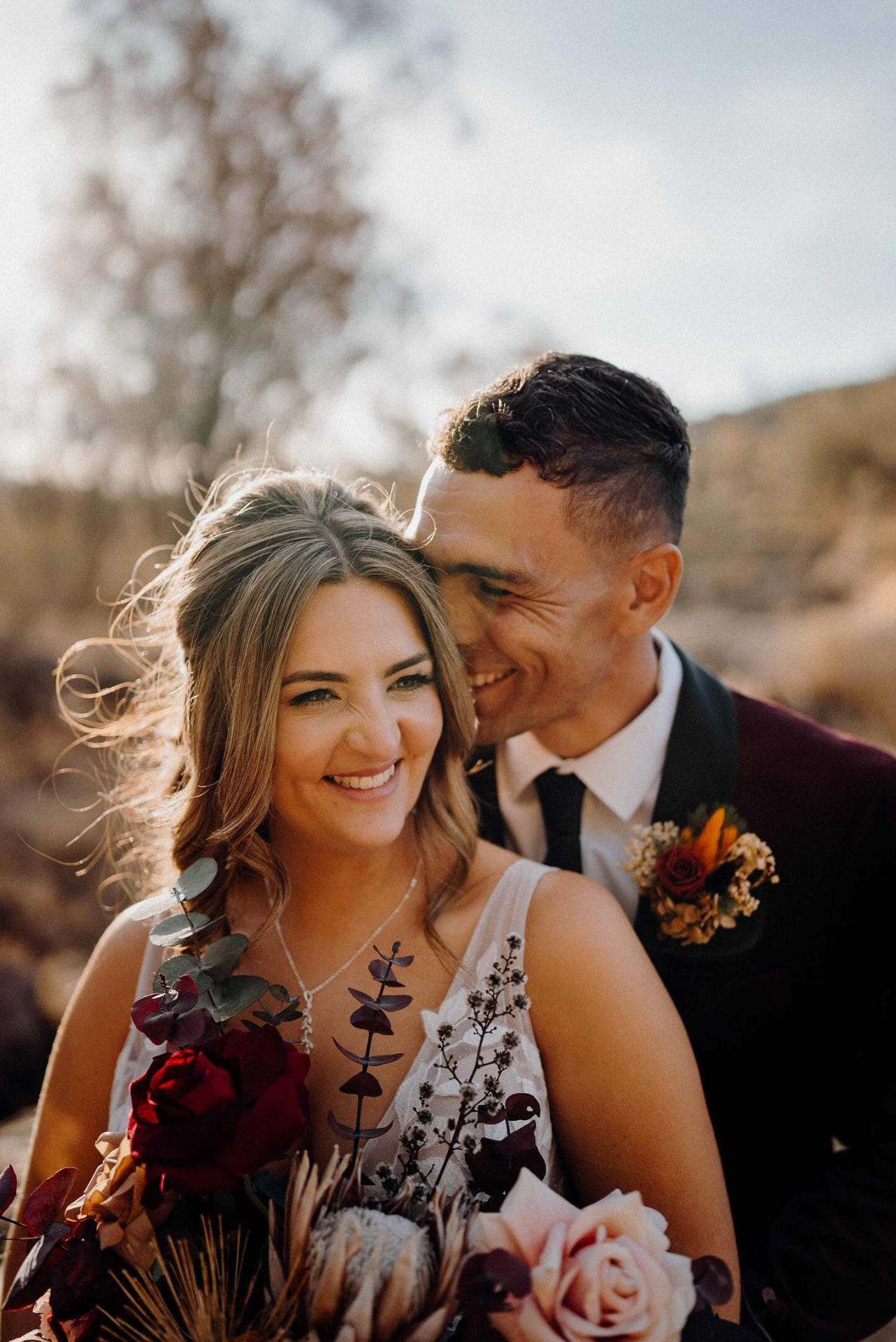 Real bride laughing with her groom at golden hour, tousled waves and warm glowing makeup