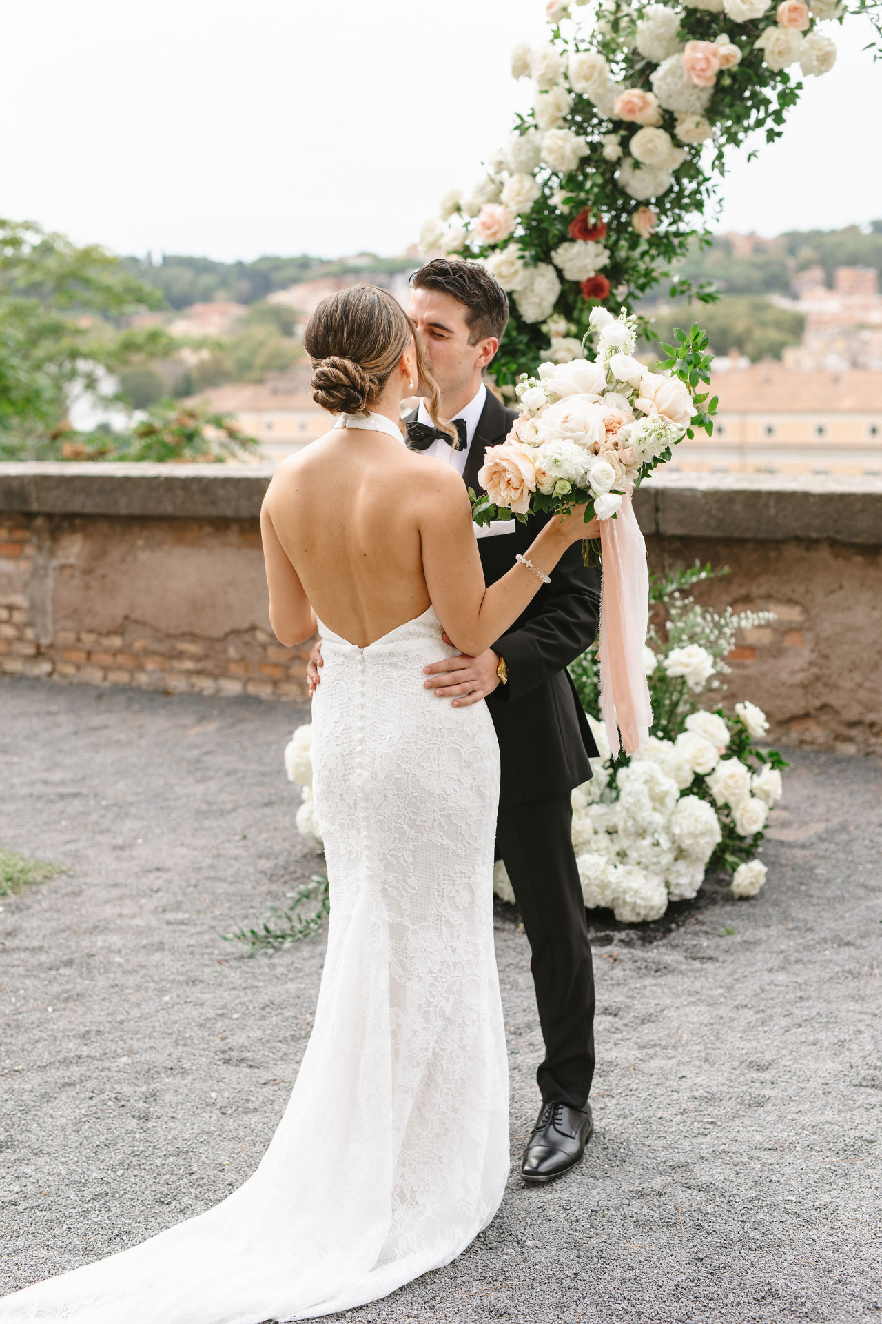 Real bride kissing her groom under a floral arch in Rome, twisted low bun bridal hair