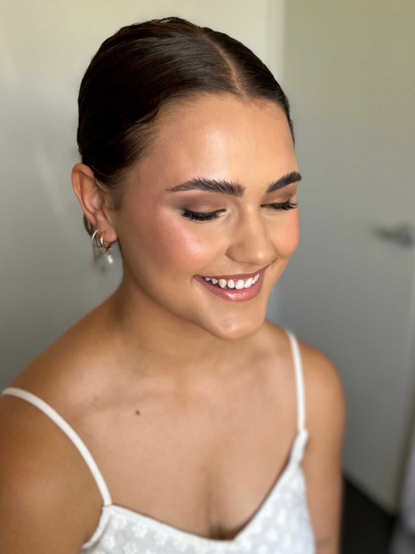 Smiling bride with a sleek centre-parted bun and warm soft glam makeup