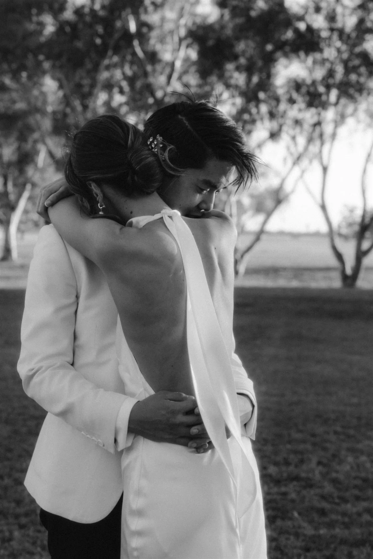 Black and white photograph of a bride and groom sharing a quiet embrace beneath the trees