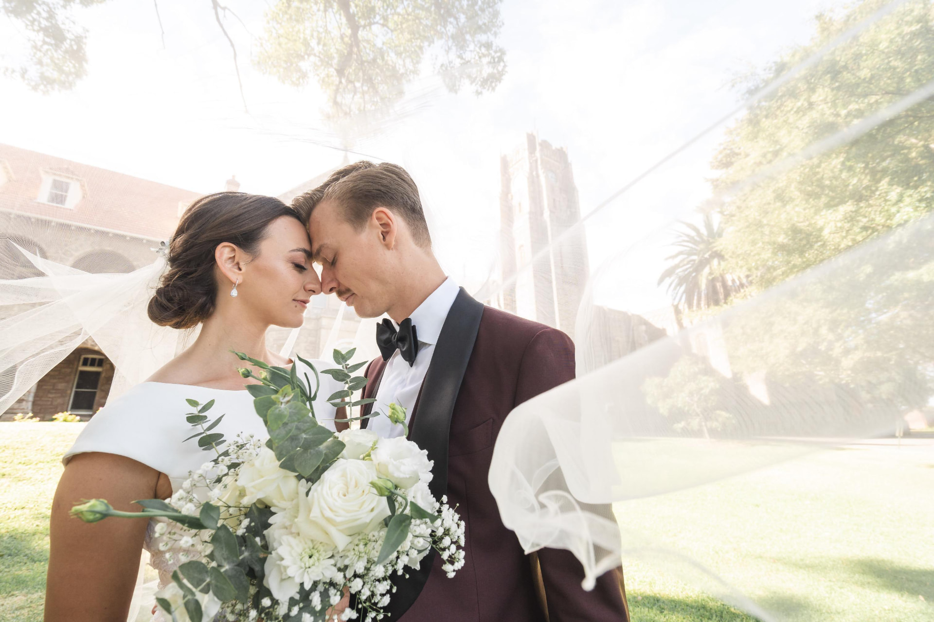 Real bride and groom forehead to forehead beneath a floating veil, soft chignon and luminous makeup