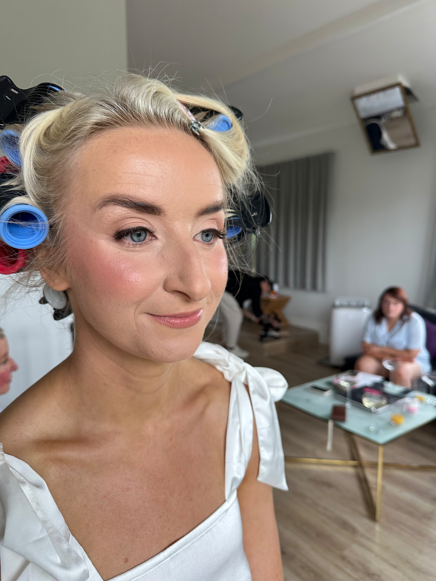 Real bride with soft glam makeup and rosy blush, hair set in rollers on her wedding morning