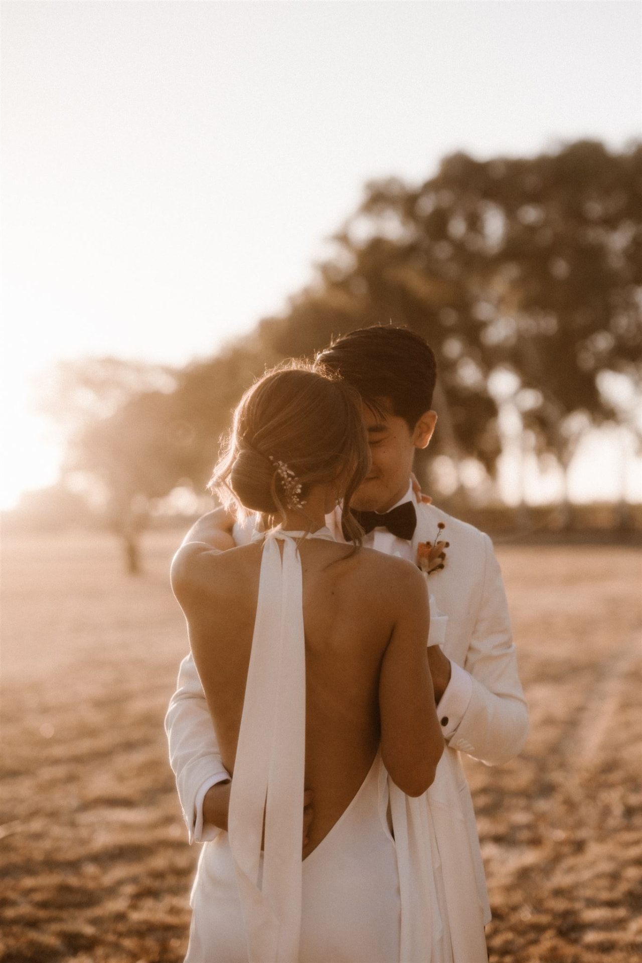 Golden hour portrait of a bride in a backless gown with a smooth low bun and delicate hairpiece