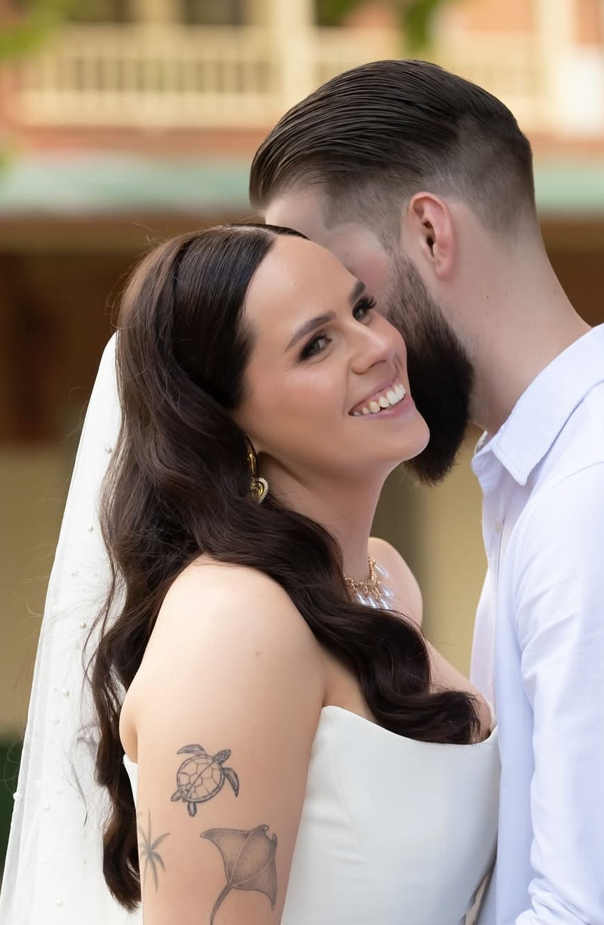 Real bride with glossy dark Hollywood waves and a pearl veil smiling beside her groom