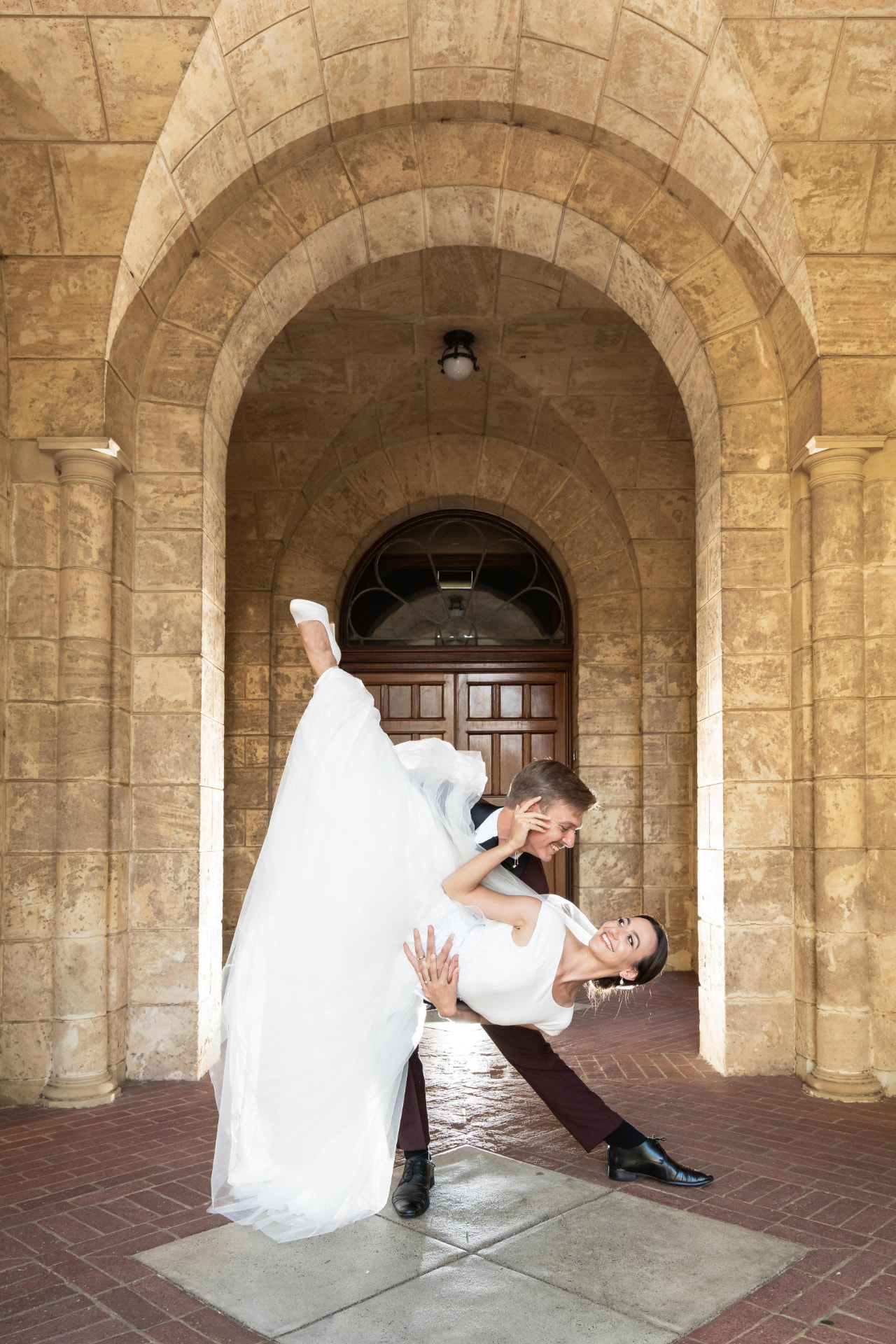 Real bride being dipped by her groom under a stone archway, sleek low bridal updo