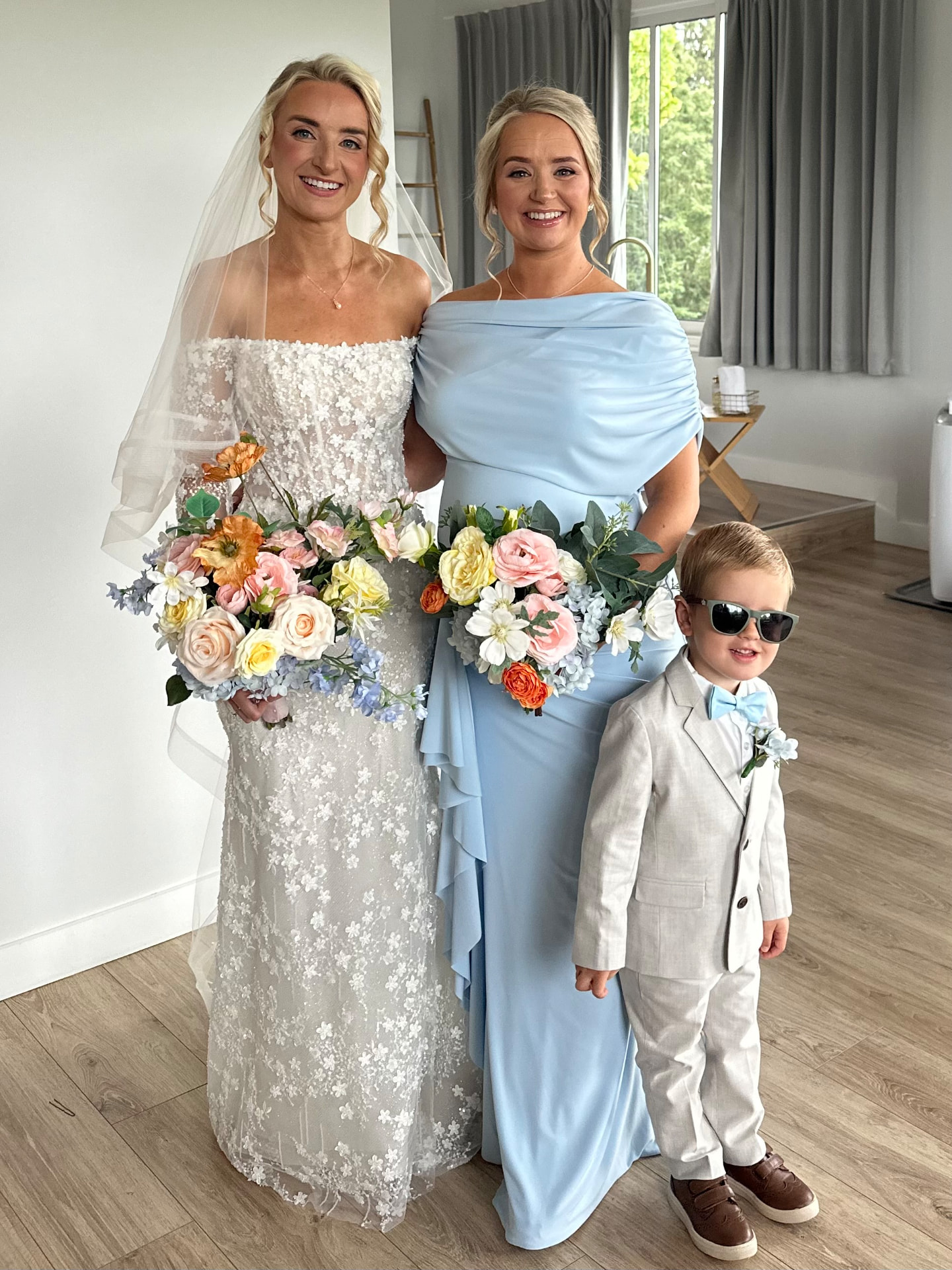 Real bride Abbi with her bridesmaid and page boy on the wedding morning, all wearing soft glam makeup and polished bridal hair